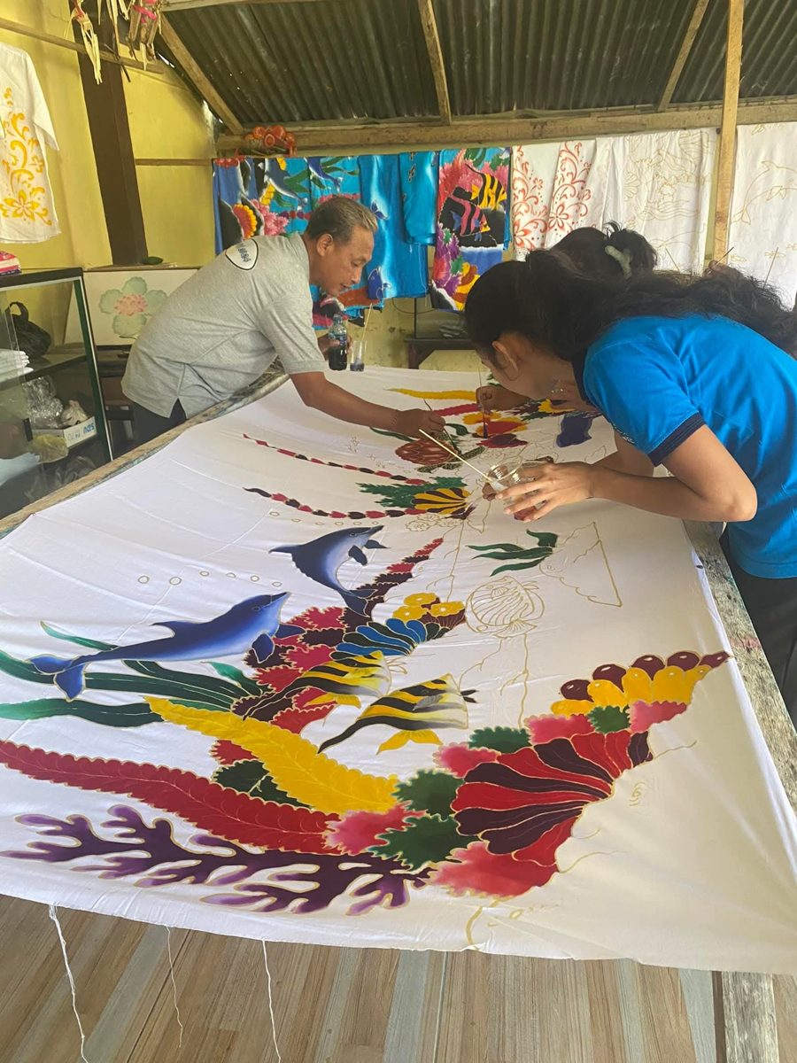 A close view of a finished batik piece featuring dolphins and coral, being painted by an instructor and student