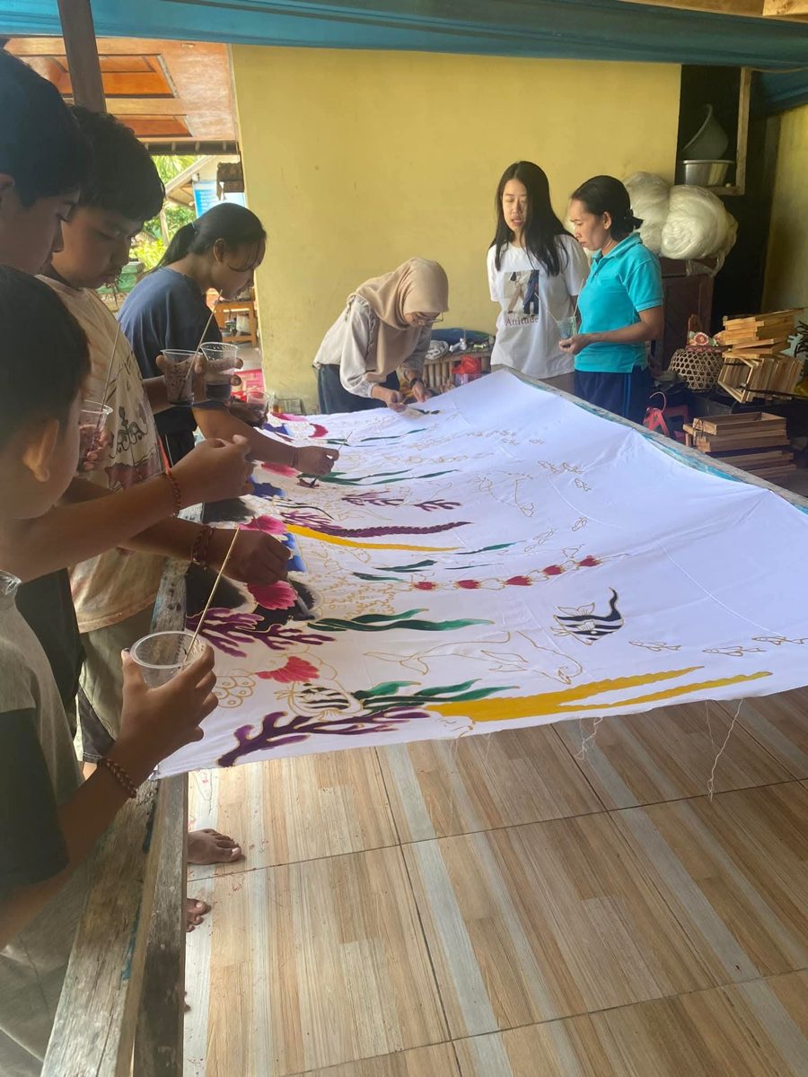 A group collaborating on a large hand-painted batik banner