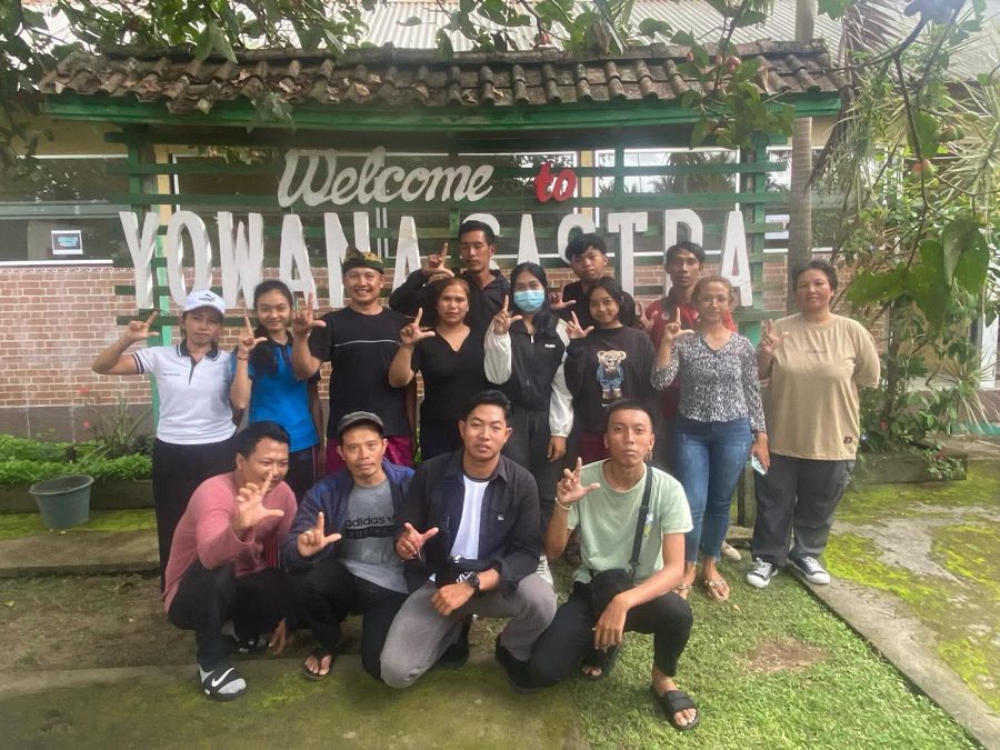 A group of program participants celebrating together in front of the Welcome to Yowana Sastra sign