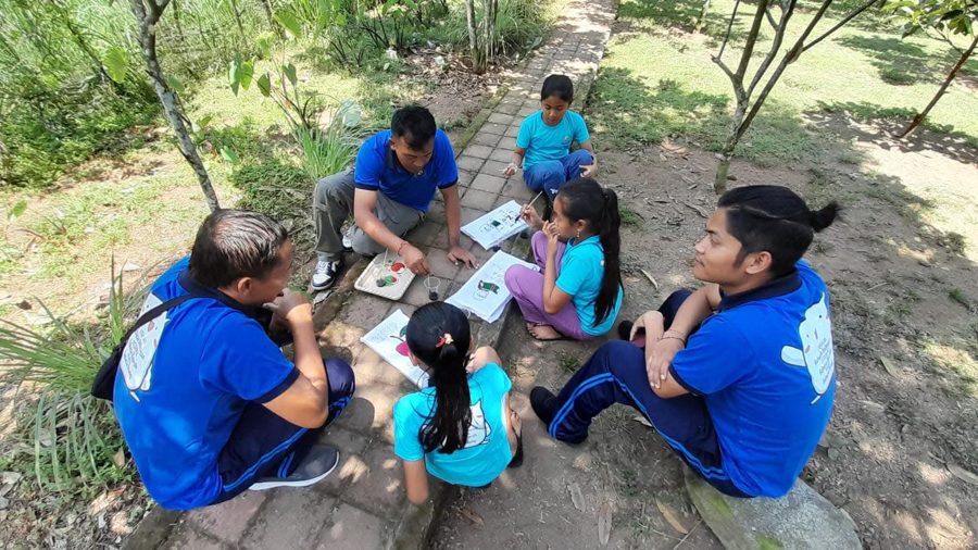 Staff mentoring a small group of students with picture cards outdoors