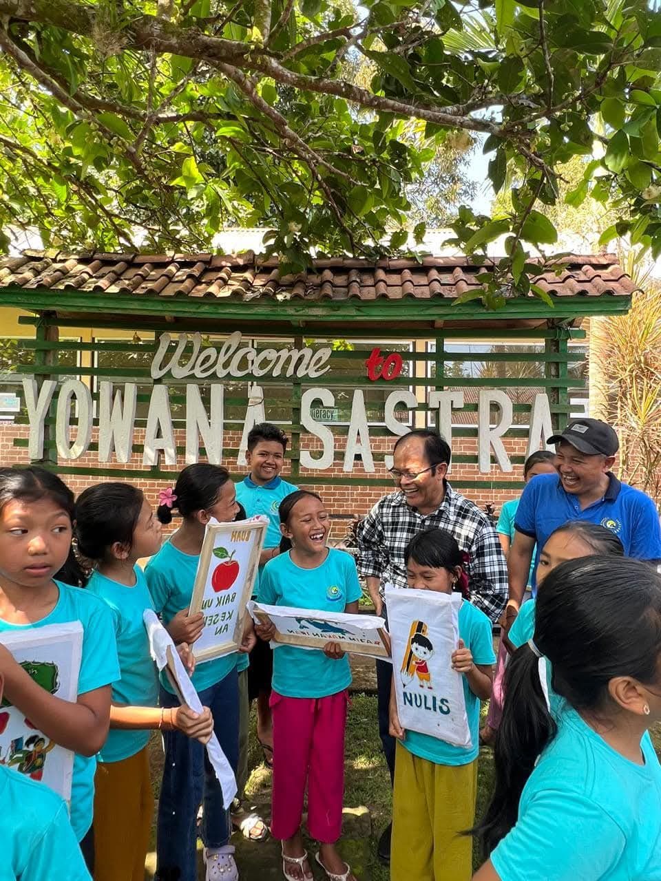 Students and staff laughing together while holding hand-painted literacy banners